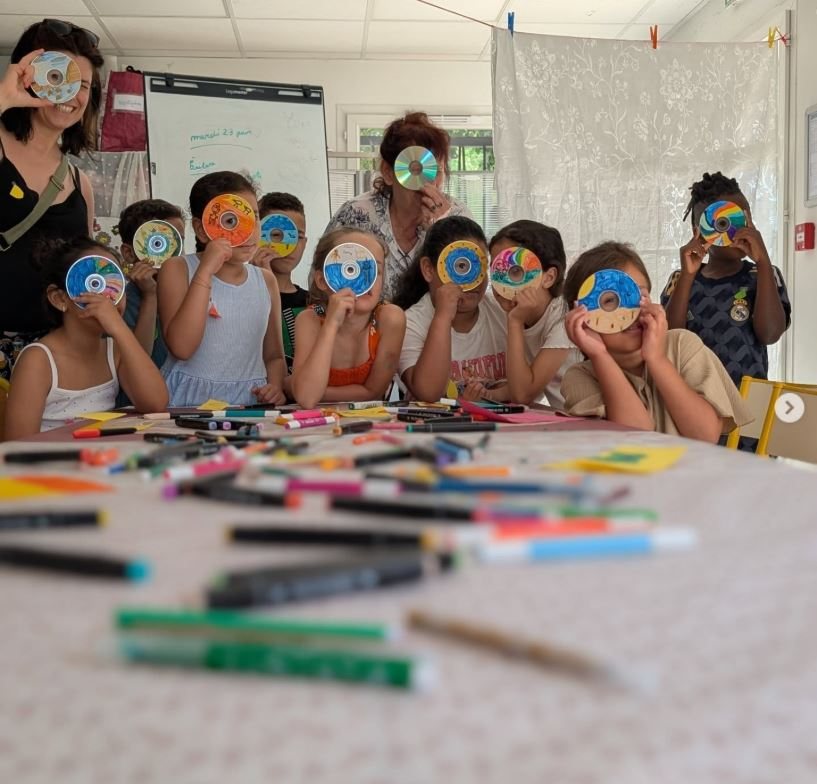 Des enfants autour d'une table d'atelier, chacun tenant un disque décoré devant son visage