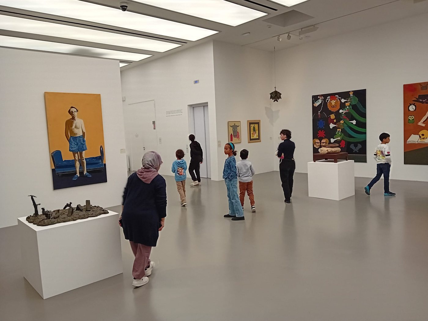 Un groupe d'enfants et d'adultes dans une salle de musée, devant de grands tableaux